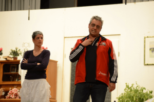 Mann in roter Sportjacke und Frau im dunklen Oberteil auf Bühne