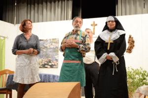 Theateraufführung: Frau, Mann mit Schürze und Nonne auf Bühne mit Monet-Gemälde