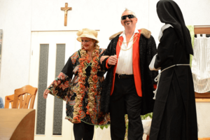 Theaterszene: Drei Darsteller in ausgefallenen Kostümen - Kimono, Showmaster und Nonne