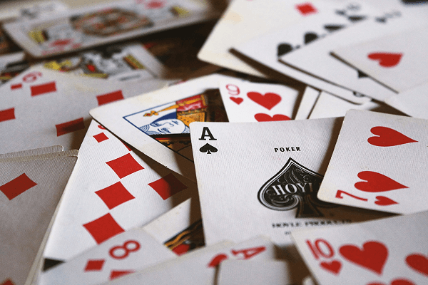 Verstreute Pokerkarten mit Pik-Ass im Zentrum, umgeben von roten Herz- und Karokarten auf Tisch